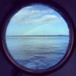 View of the ocean and a rainbow through a porthole