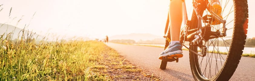 A person's leg on a bicycle with a green field on a sunny day