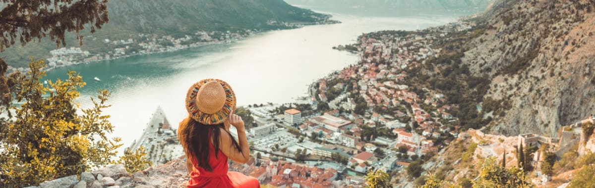 Young lady in a sunhat and red dress over looking the city from a cliff